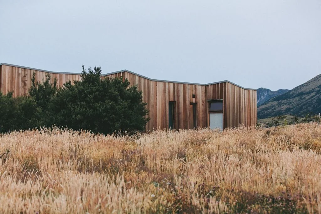 ADU design reference showing a low timber-clad building in a grassy landscape.