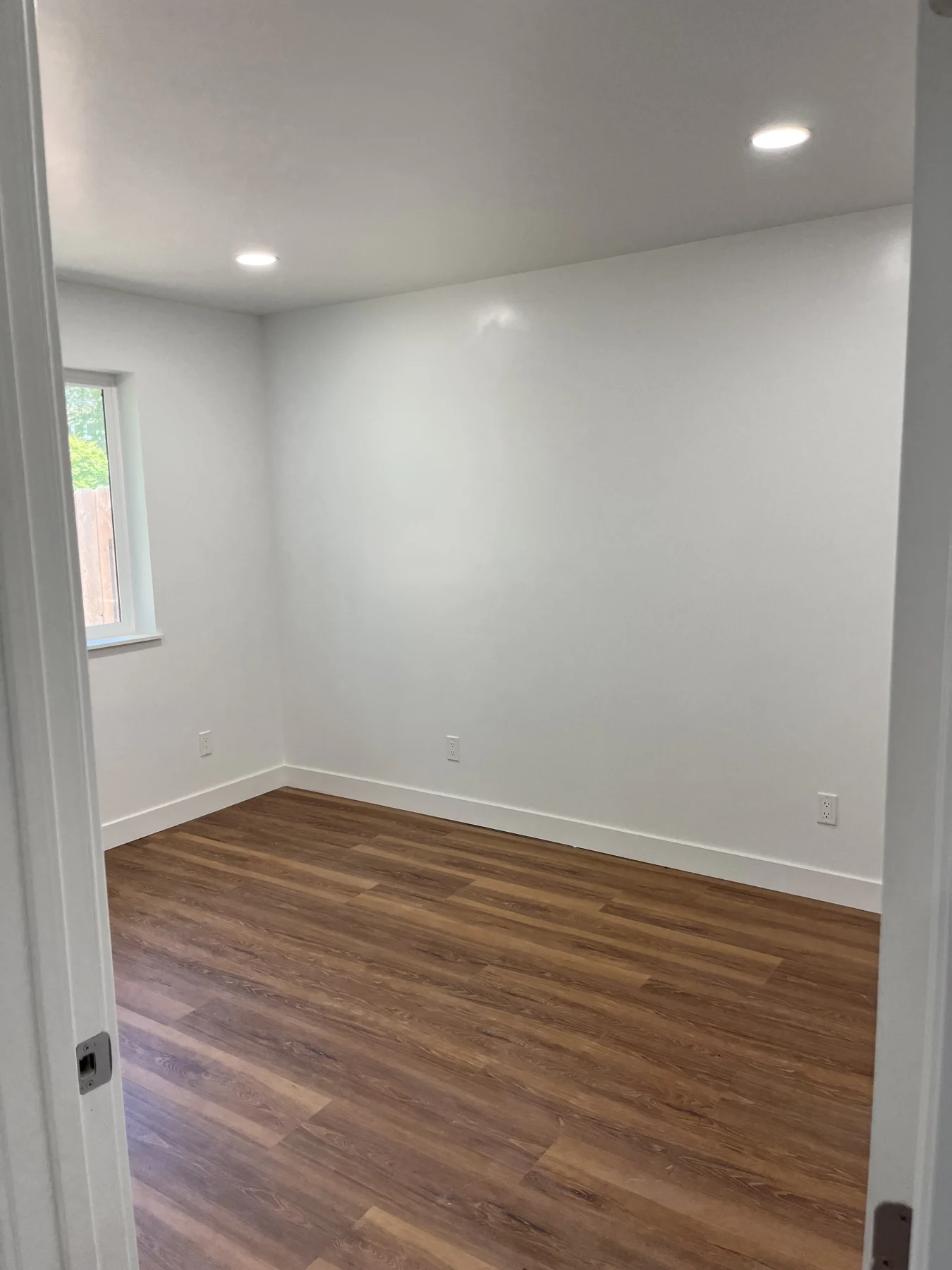 ADU room with white walls, wood-look flooring and a window.