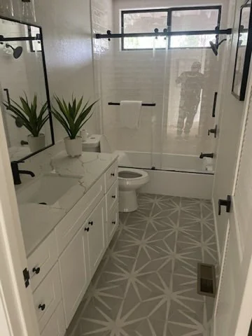 Bathroom with a white vanity, patterned floor and tub-shower enclosure.