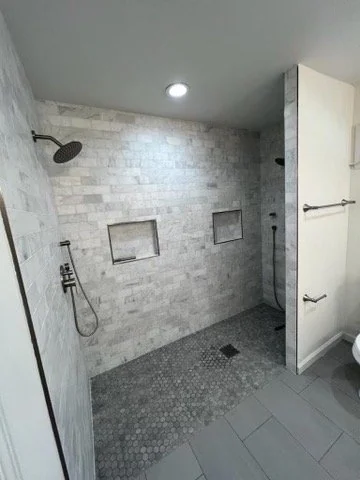 Walk-in shower with gray tile, a recessed niche and dark fixtures.