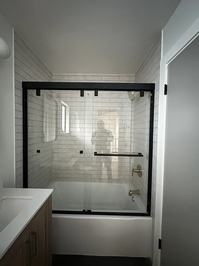 Bathroom with a glass shower screen, pale tile and wood vanity.