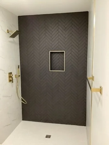 Walk-in shower with dark accent tile, a recessed niche and gold fixtures.