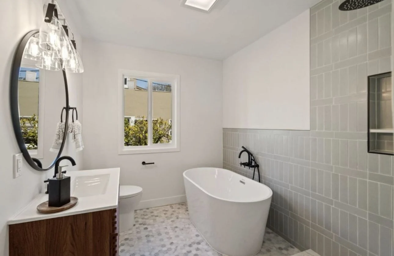 Bathroom detail with a freestanding tub, round mirror and wood vanity.