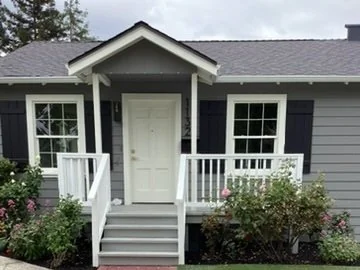 Gray bungalow exterior with white trim, a front porch and brick walkway.