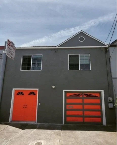 Dark painted house exterior with a red entry door and garage door.