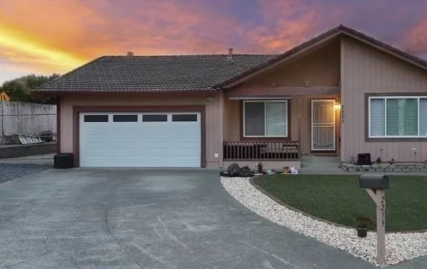 Single-story painted house with a garage and front landscaping at sunset.