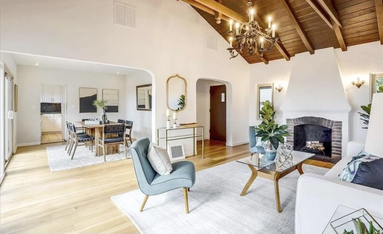 Living room with exposed beams, a fireplace and a view into the dining area.