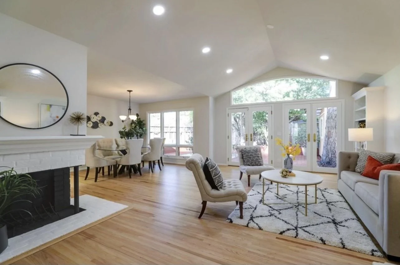 Living area with pale walls, a large round mirror and broad garden windows.