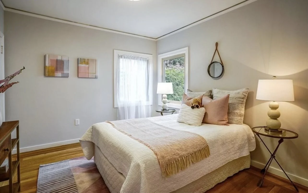 Bedroom with warm pale walls, a white bed and dark bedside furniture.