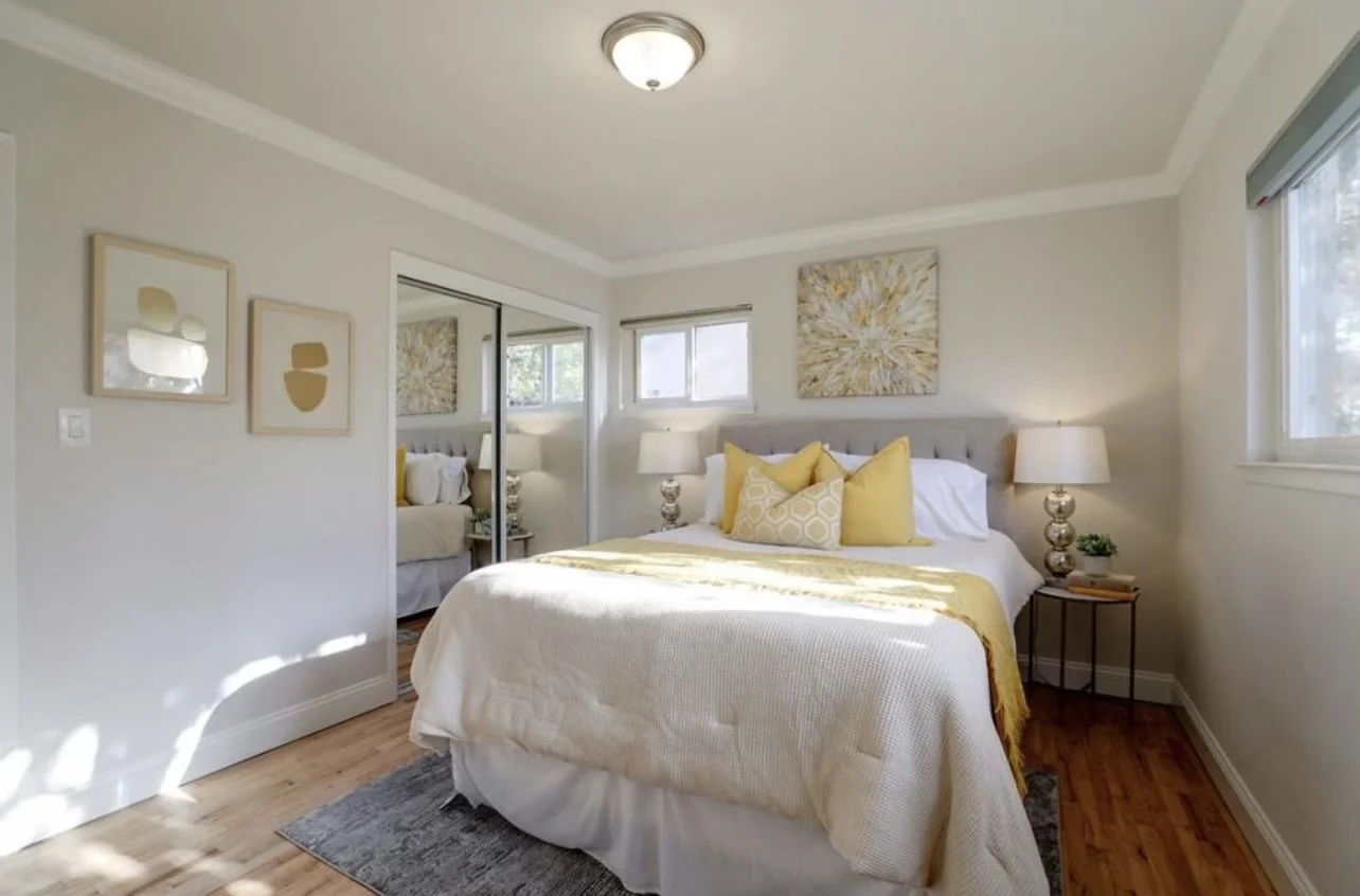 Bedroom with pale walls, a yellow throw and windows above the bed.