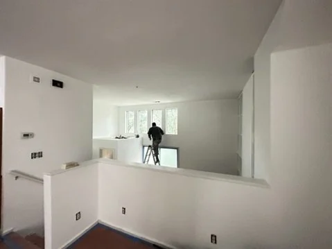 Interior painting work in progress around white walls and an open stairwell.