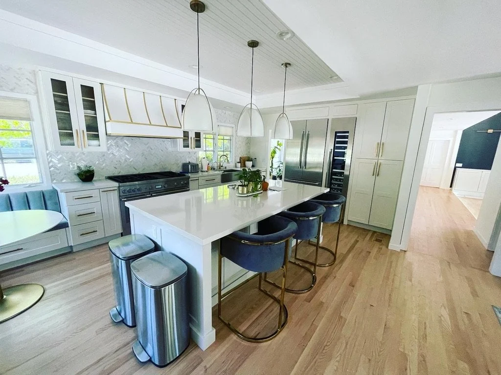 White kitchen with a large island, dark stools and pendant lights.