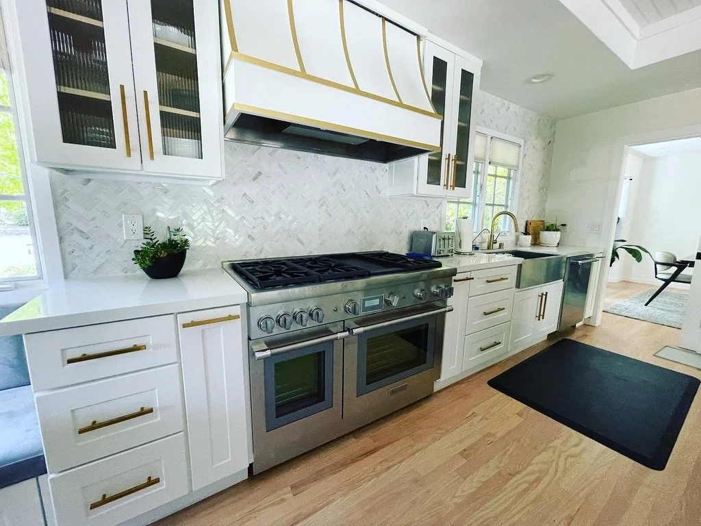 White kitchen with a dark range, patterned backsplash and windows above the counter.