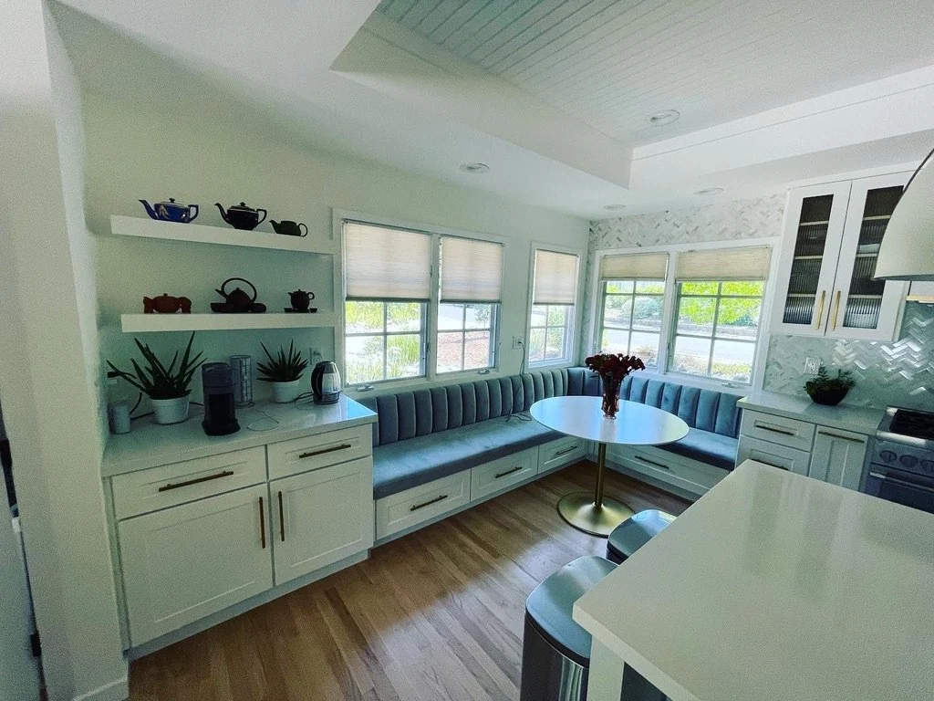 White kitchen with built-in window seating and a round dining table.
