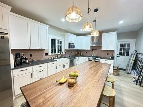 White kitchen with a wood island, fruit bowl and woven pendant lights.
