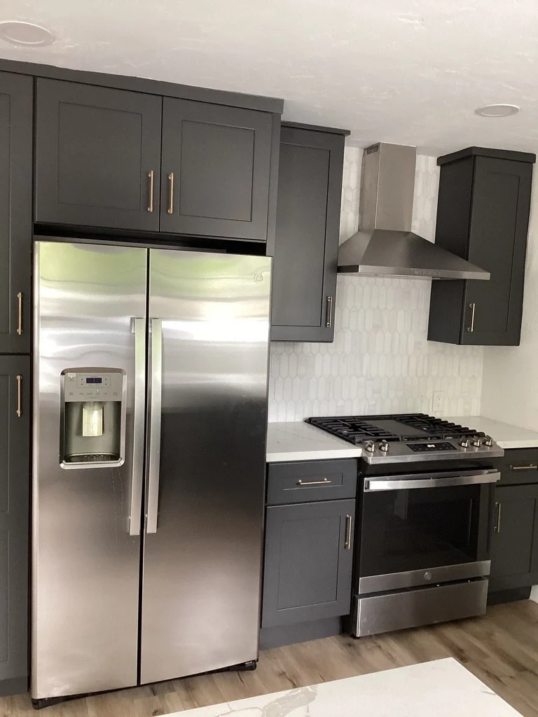 Kitchen with charcoal cabinets, white counters and stainless appliances.